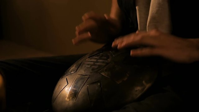 Man playing tank drum or hang at home. Warm romantic illumination, low key. Relaxation, meditative and traditional music concept. Close up shot