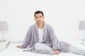 Relaxed young man in bathrobe sitting on bed