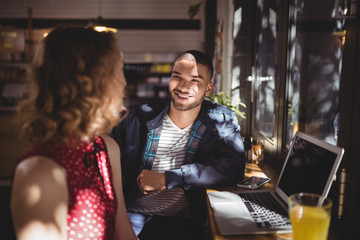 Smiling young man talking with female friend sitting at coffee shop