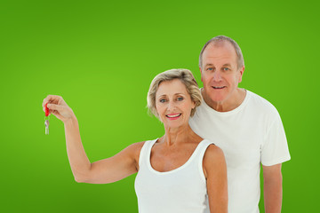 Mature couple smiling at camera with new house key against green vignette