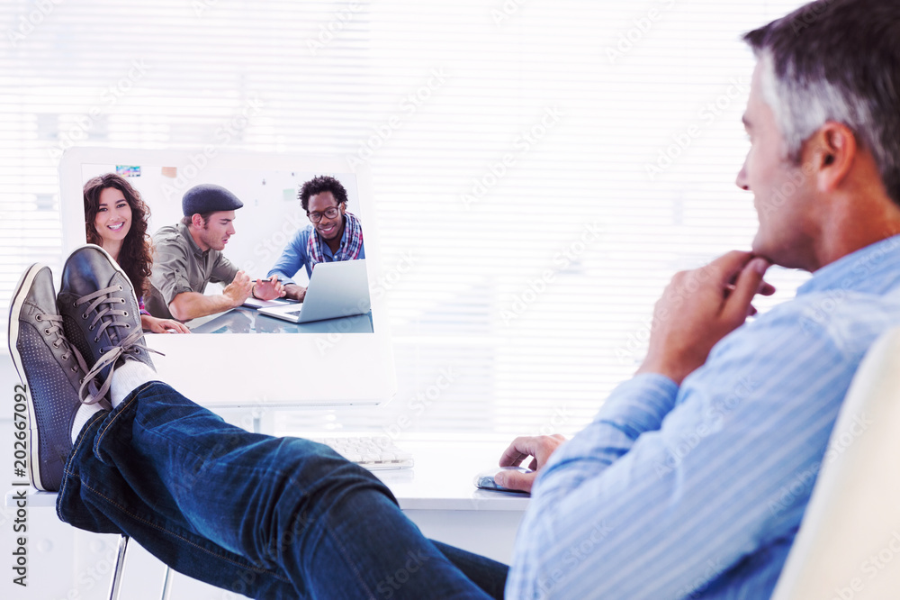 Poster relaxed man with feet on desk using computer against creative team working together with one smiling