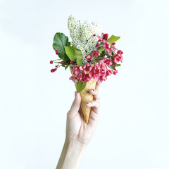 Woman's hand holding a waffle cone with spring flowers bouquet on the bright background. Flat lay, top view. Mothers day, anniversary,  greetings.