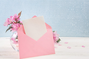 Сard with an pink envelope and pink flowers of apple tree on wooden board.