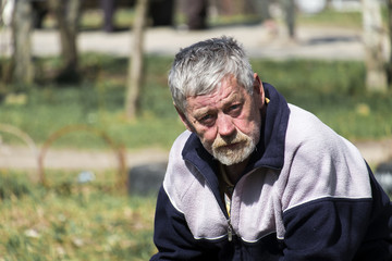 Gray-haired bearded old man sitting on a bench and looks
