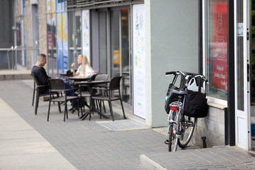 Rower z torbami przed sklepem, kobieta i mężczyzna przy stoliku przed restauracją.
