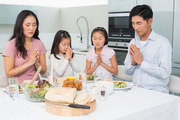 Family of four saying grace before meal in kitchen