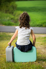une fillette brune,attend, assise sur une valise en tenant une autre dans sa main