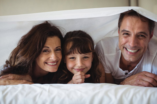 Parents and daughter smiling under the bed sheet