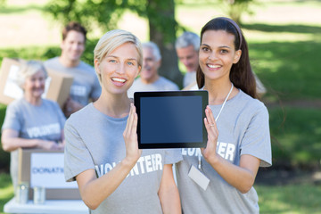 Happy volunteer friends showing tablet pc screen