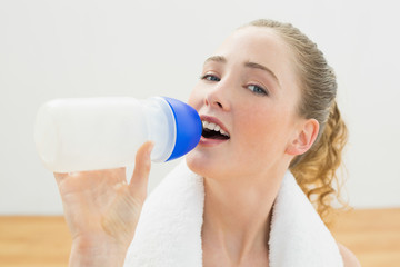 Happy slim blonde sitting on floor drinking from sports bottle