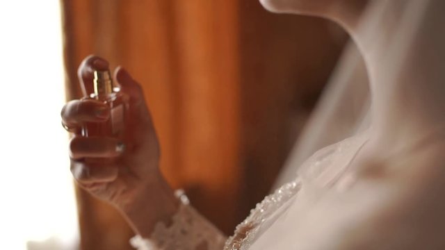 The bride gently spray perfume around his neck. The video is slower. Still shot in the backlight. Slow motion