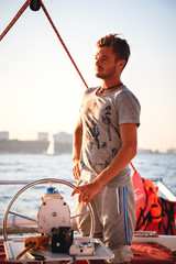 Young handsome man, captain driving yacht in sea at sunny day