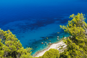 Beautiful turquoise color of sea water is seen through the foliage of trees on Pefkoulia Beach, Lefkada island or Lefkas, Greece. Idyllic sunny day.