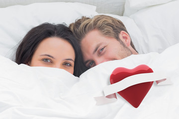 Couple hiding under the duvet against heart with scroll