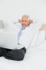 Relaxed businessman looking at laptop in bed