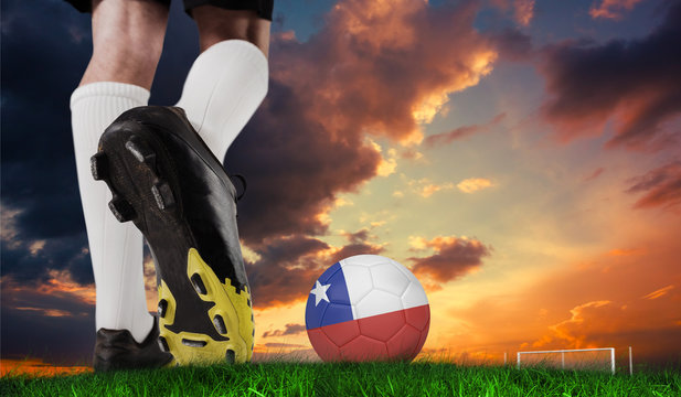 Composite image of football boot kicking chile ball against green grass under dark blue and orange sky