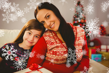 Festive mother and daughter holding christmas present against snowflakes