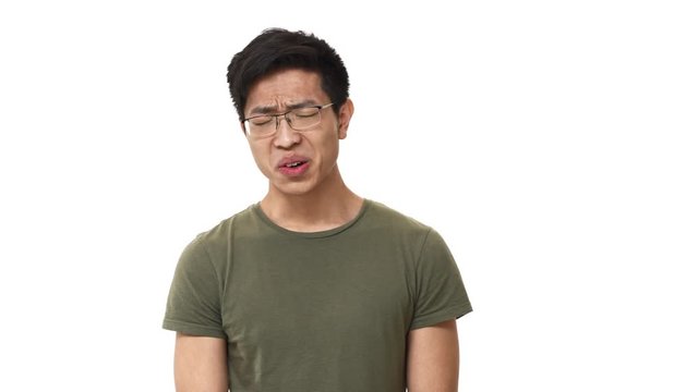 Portrait of displeased asian man 20s wearing glasses frowning while expressing disgust and aversion, isolated over white background. Concept of emotions