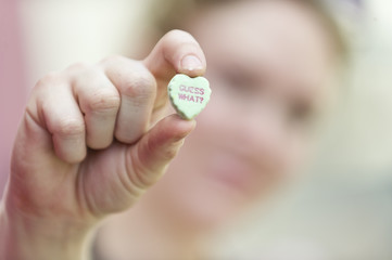 Closeup focus of woman holding candy heart that says guess what