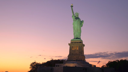 CLOSE UP Famous Statue of Liberty lit up with lights against fiery sky at sunset © helivideo