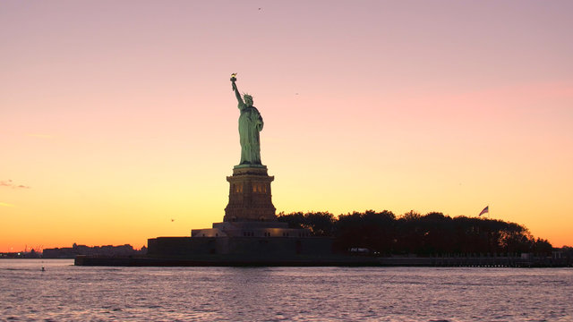 LOW ANGLE: Iconic Statue of Liberty against gorgeous fiery orange sunset sky