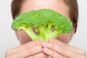 Fototapeta na wymiar Woman holds broccoli with her hands in front of her face