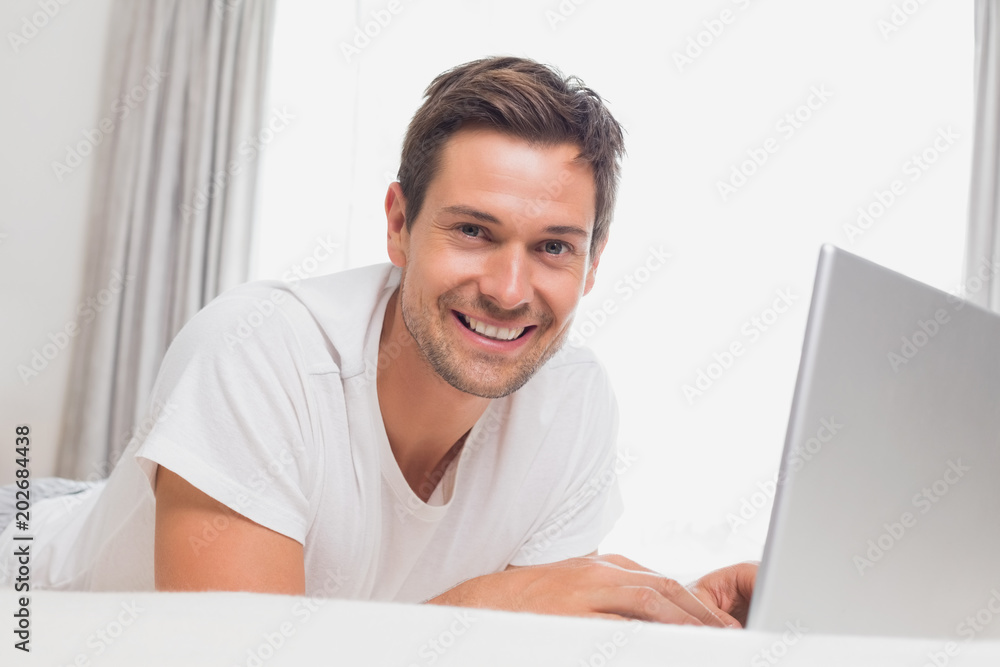 Wall mural portrait of relaxed casual man using laptop in bed