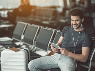 Portrait of beaming bearded man hearing song while using appliance in airport