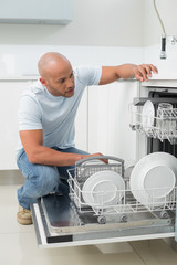 Serious man using dish washer in kitchen