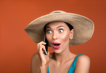 Portrait of woman being shocked while speaking by cellphone. Sunhat is on her head. Isolated on background