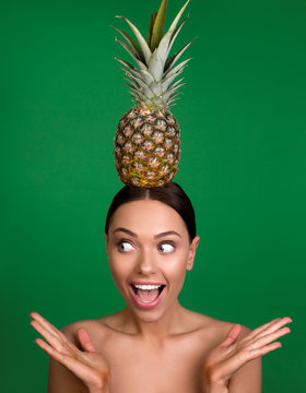 Portrait of naked girl with astonished expression keeping pineapple on the top of her head. Isolated on background