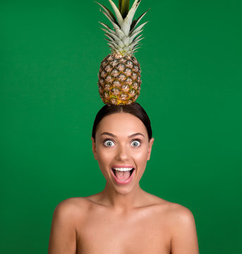 Portrait of content lady with undressed upper body holding pineapple on head. Isolated on background