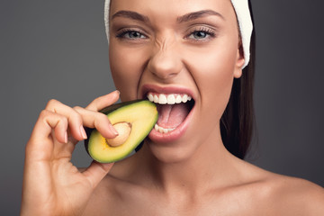 Close up of starving woman with perfect skin biting ripe avocado. Isolated on background