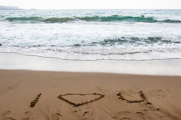 I love you drawn in the sand of a Greek beach with turquoise water in a cloudy day