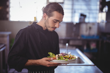 Young waiter holding fresh salad plate in commercial kitchen
