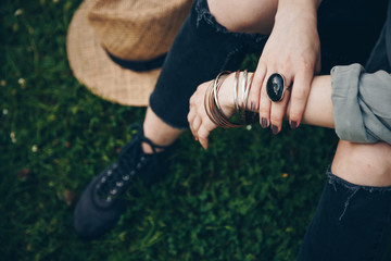 close-up of a woman wearing ring, bracelets and listening to music on her smartphone. street style detail of a boho-chic music festival female accessories. ideal summer outfit. girl sitting on grass