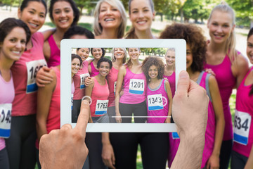 Composite image of hand holding tablet pc showing photograph of breast cancer activists