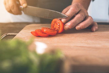 Close up of senior female arms chopping fresh red vegetable by knife in kitchen