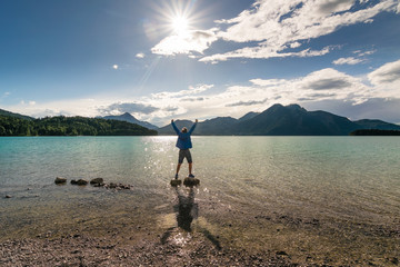 Tourist steht mit Emotion auf einem Stein am See in den Bergen