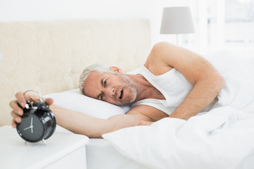 Obraz na płótnie Canvas Mature man extending hand to alarm clock in bed