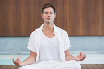 Handsome man in white meditating in lotus pose