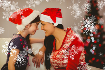 Obraz premium Festive mother and daughter smiling at each other against snowflakes