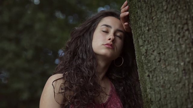 Pensive sad young brunette leaning against a tree