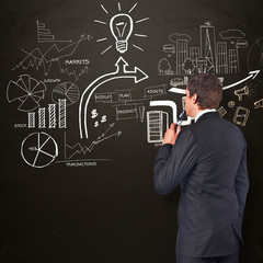 Thinking businessman holding glasses against blackboard