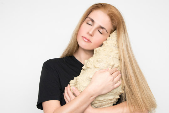 Gorgeous blonde woman holds a giant clam to her ear and listens