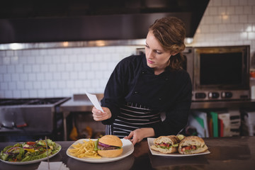 Confident young waiter holding paper while standing with fresh meal at counter