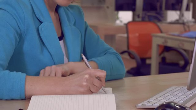 unrecognizable woman writing notes or to do list in notebook sitting at the wooden desk