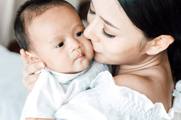 Mother holding baby in her arms and kiss in a white bedroom.Love of family concept