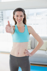 Toned woman gesturing thumbs up in fitness studio