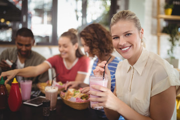 Portrait of smiling young woman holding milkshake at cafe